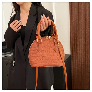 Bolso concha marrón naranja con textura de cocodrillo llevado por modelo en traje negro