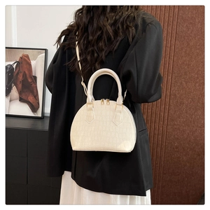 Detalle de bolso tipo concha beige con textura de cocodrilo y correa de hombro ajustable