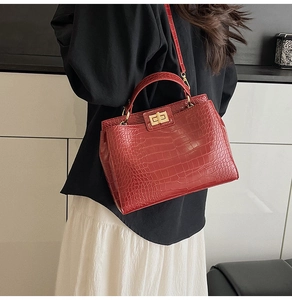 Detail of red crocodile pattern handbag with gold clasp shown on a model's arm