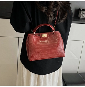 Detail of red crocodile texture handbag with gold twist lock worn as crossbody