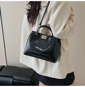 Detail of black crocodile texture handbag with gold twist lock on a white blazer