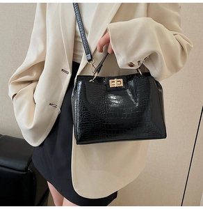 Close-up of black crocodile pattern leather handbag with gold twist lock and strap