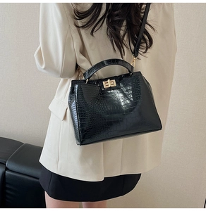 Side view of black faux crocodile leather handbag with gold twist lock on beige blazer
