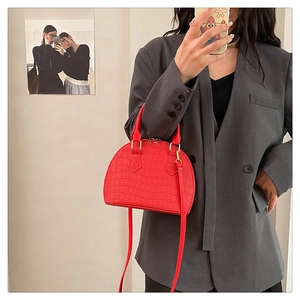Detalle de bolso rojo tipo concha con grabado de cocodrilo, cremallera dorada y asa