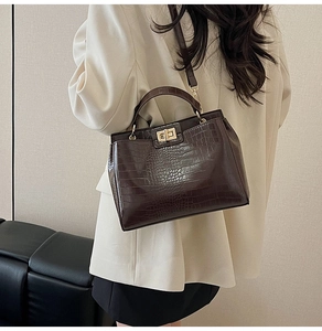 Detail of dark brown crocodile pattern handbag with gold clasp on a female model