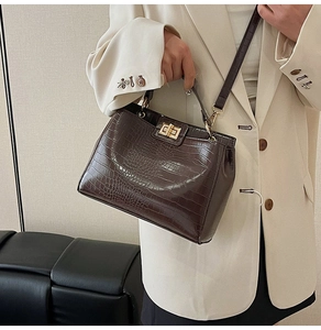 Detail of dark brown crocodile pattern handbag with golden twist lock and top handle