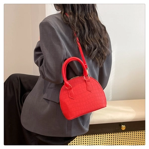 Modelo luciendo bolso de concha rojo con textura de cocodrilo, asas superiores y bandolera