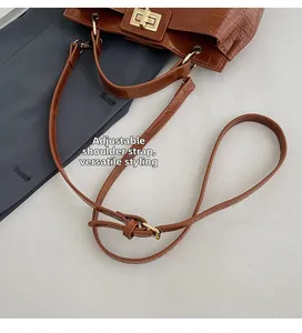 Detail of adjustable strap and golden metal clasp on brown crocodile pattern handbag