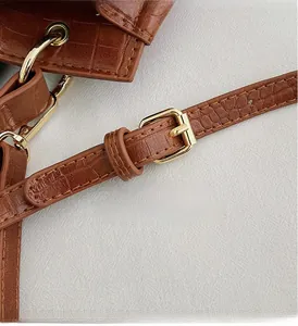 Detail of brown crocodile pattern handbag showing golden metal strap buckle and stitching