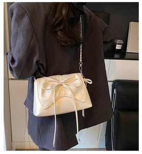 Detail of cream white pleated shoulder bag with large bow and silver metal chain strap