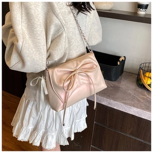 Pink crossbody bag with large bow and chain strap displayed in a modern interior