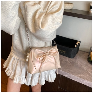 Detail of champagne gold ballet bow bag with silver chain strap shown in a modern interior