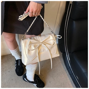 Detail of a creamy white crossbody bag featuring a large bow and silver chain strap