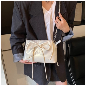 Detail of elegant cream shoulder bag featuring a large bow and metallic chain strap