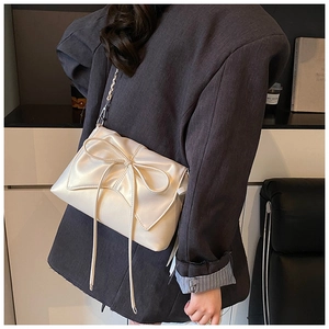 Detail of a chic cream ballet-style crossbody bag with a large bow and chain strap