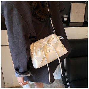 Detail of a pearl white bow bag with silver chain strap worn over a black blazer