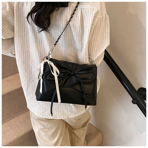 Close-up of black crossbody bag with bow pleats and white ribbon on chain strap