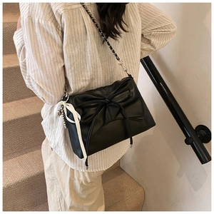 Detail of black leather crossbody bag with bow design and silver chain strap on model