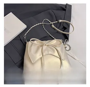 Detail showing the cream-colored pearl leather texture and large bow on the handbag