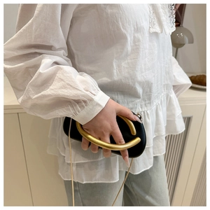 Macro detail of black matte leather clutch with large gold metal ring handle and chain