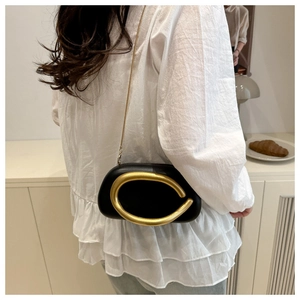 Detail of black PU leather crossbody bag with bold gold C-shaped metal buckle and chain