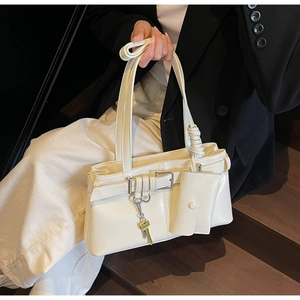 Close-up of minimalist cream white shoulder bag with decorative strap and gold key charm