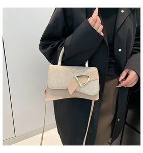 Detail of beige crossbody bag featuring textured lid and golden D-shaped metal clasp buckle