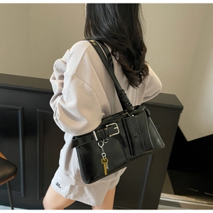 Model wearing a black glossy leather underarm bag with silver key charm and front pocket