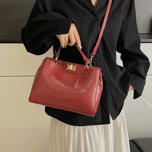 Red crocodile embossed handbag with gold clasp carried by model in white dress