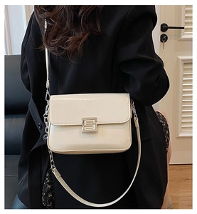 Detail of cream white leather bag showing geometric gold buckle and chain strap