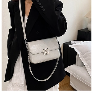 Close-up of a cream leather crossbody bag with a silver S-shaped buckle and chain strap