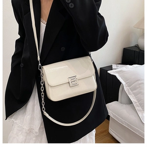 Close-up of cream patent leather bag featuring silver S-buckle and fine chain detail