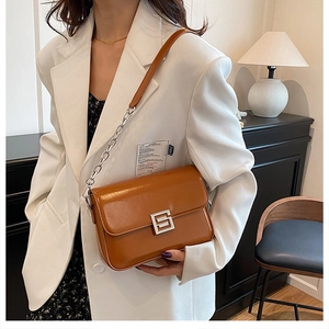 Detail of brown leather crossbody bag with silver chain strap on white blazer