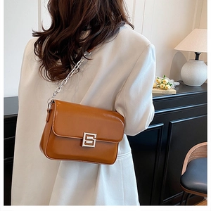 Detailed close-up of brown glossy leather bag with silver chain and geometric buckle
