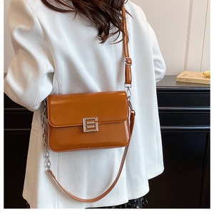 Detail of caramel faux leather bag with silver buckle and chain strap on white blazer