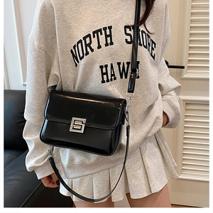 Detail view of a black glossy shoulder bag featuring a square silver metal buckle and strap