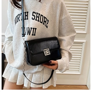 Model wearing a black glossy shoulder bag with silver geometric buckle and chain strap
