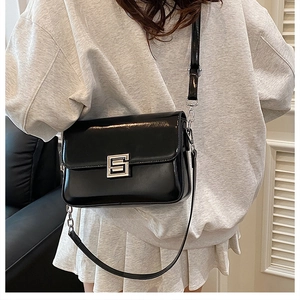 Close-up of a retro black glossy leather shoulder bag with a silver rectangular buckle