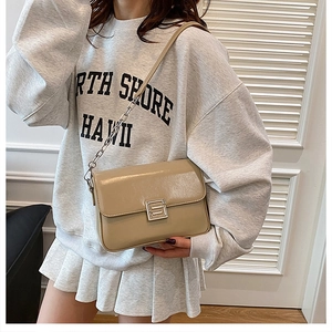 Close-up of khaki shoulder bag with silver S-shaped buckle and chain strap on model