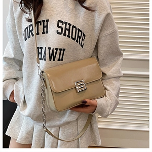 Detail of light khaki patent leather crossbody bag with silver S-shaped buckle and chain strap