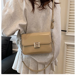 Detail of square beige crossbody bag featuring silver buckle and chain strap on model