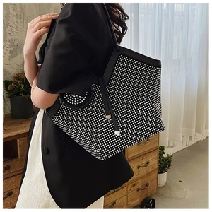 Close-up of a large black rhinestone tote bag worn by a model in a stylish interior