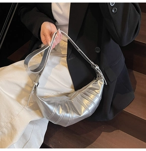 Detail of silver metallic croissant bag showing textured pleats and shoulder strap