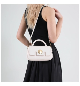 Side view of cream crossbody bag with gold metal buckle on a model wearing black dress