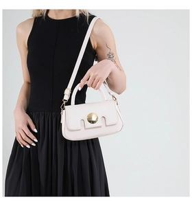 Minimalist white crossbody bag with round gold buckle shown on model in black dress