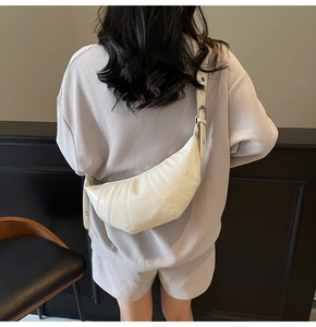 Close-up of cream pleated crescent bag with wide adjustable strap and metal eyelets