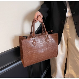 Close-up of brown crocodile embossed leather tote bag with elegant gold metal ring hardware