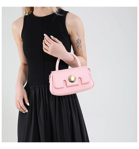 Petit sac carré rose avec boucle dorée porté par un mannequin en robe noire chic