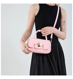 Pink leather crossbody bag with gold round buckle shown on a model in a black dress