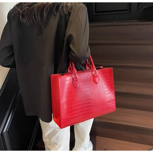 Deep red crocodile embossed tote bag held by a model in a black suit for professional style